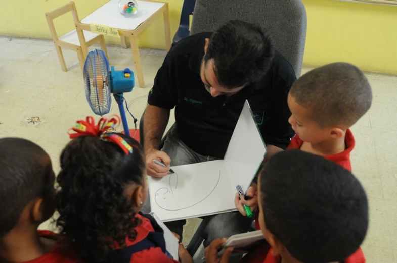 a man drawing on a sheet of paper to children