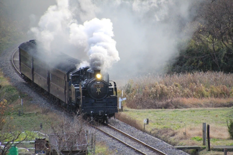 a steam train moves along tracks as it emits white smoke