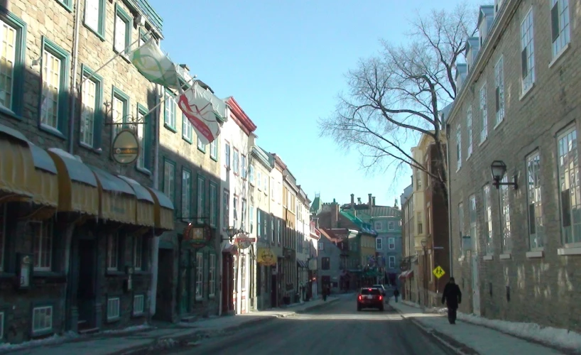 a street with parked cars, buildings, and a man walking