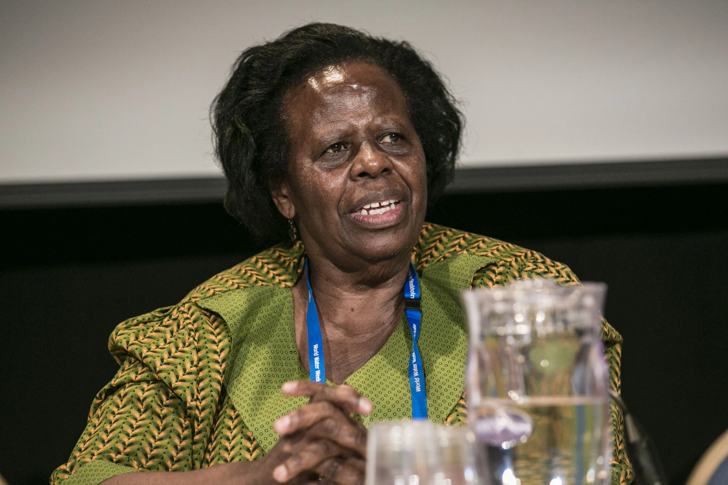 a woman sitting at a table talking with a blue lanyard around her