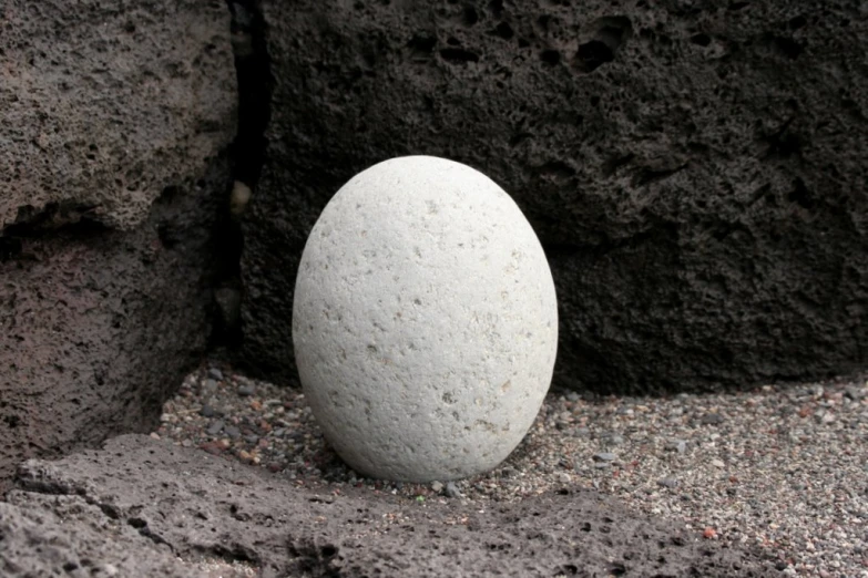 a rock sitting in the middle of cement with a white egg in it