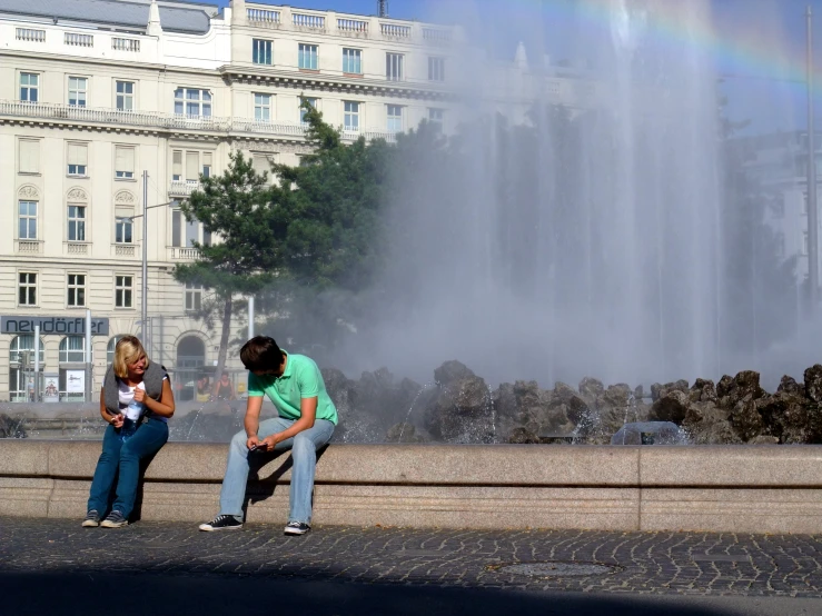 people sitting on the side of a lake under a rainbow