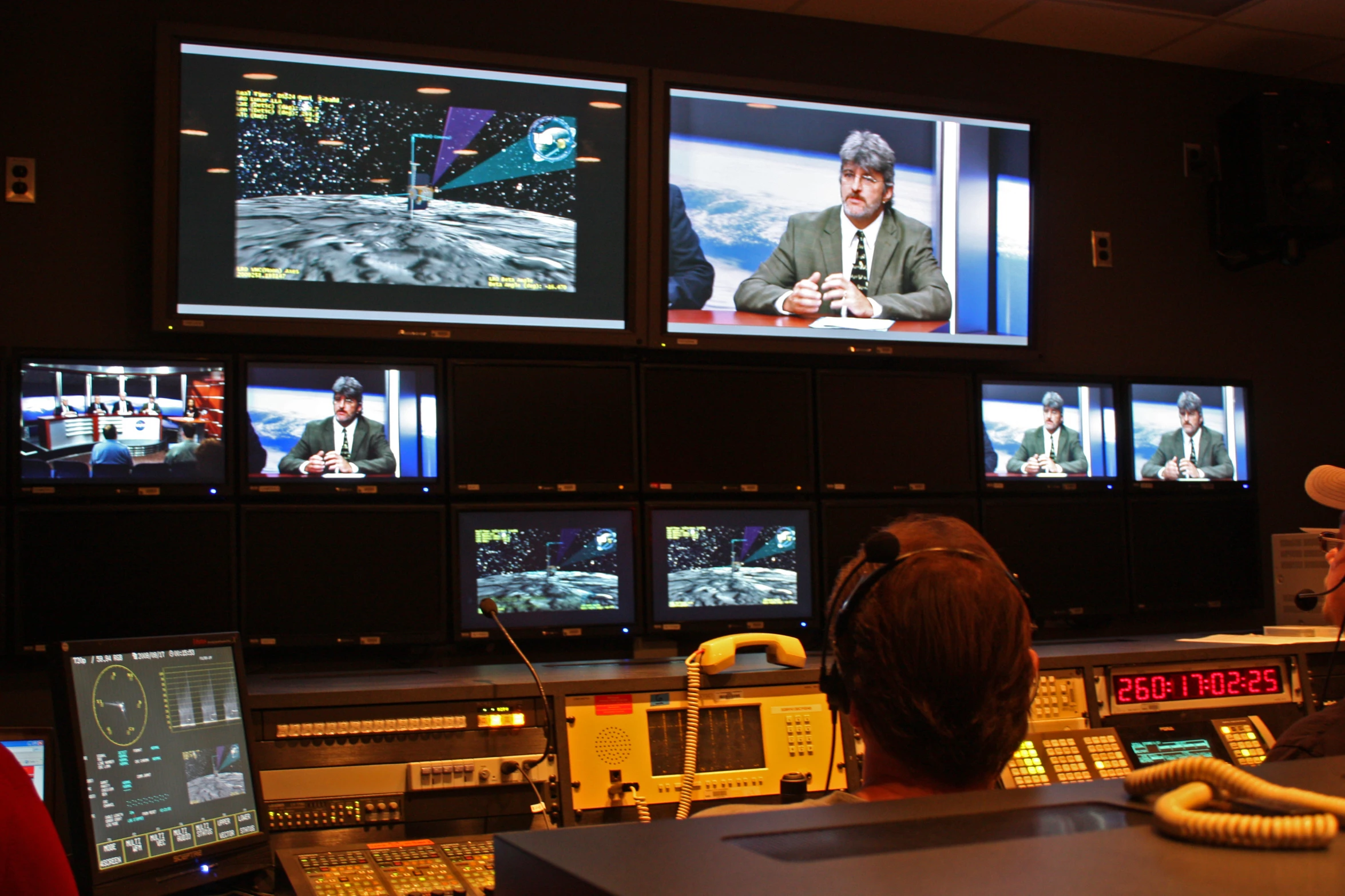 several large monitors are shown while a man is sitting down at the phone