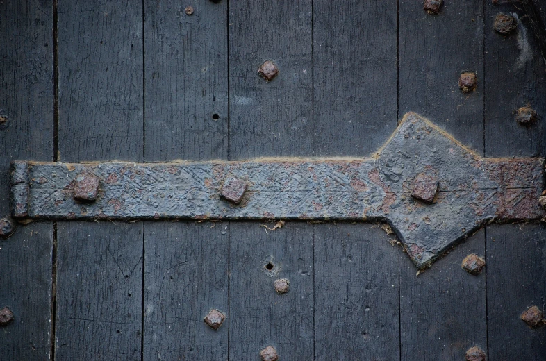 a grungy blue arrow with holes attached to the side of an old building