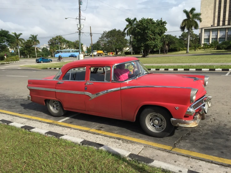 an old red car sitting on the side of a road