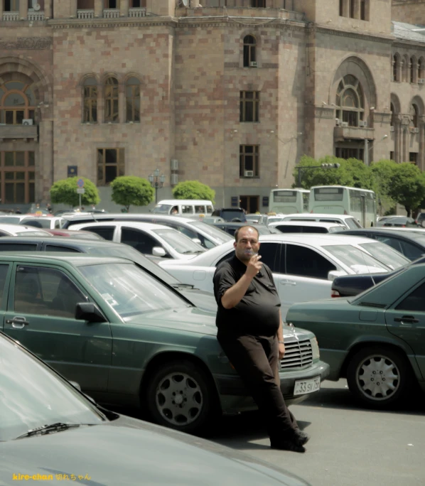 an obese man talks on his cell phone while standing in the parking lot