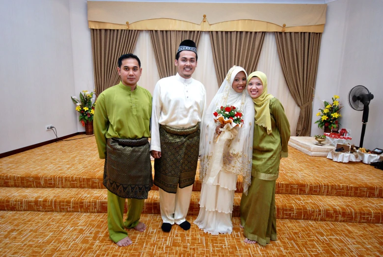 three adults and one child stand together in front of a carpeted stage with flower arrangements