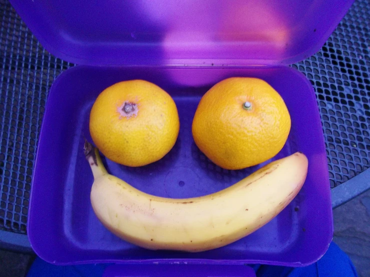 an orange and a banana in a purple container with smiling face