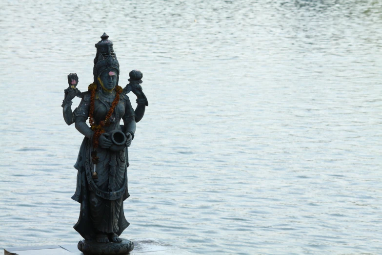 a statue of an indian woman with a crown standing on the edge of a body of water