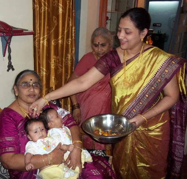 a woman in a sari is holding a baby and is standing next to her family