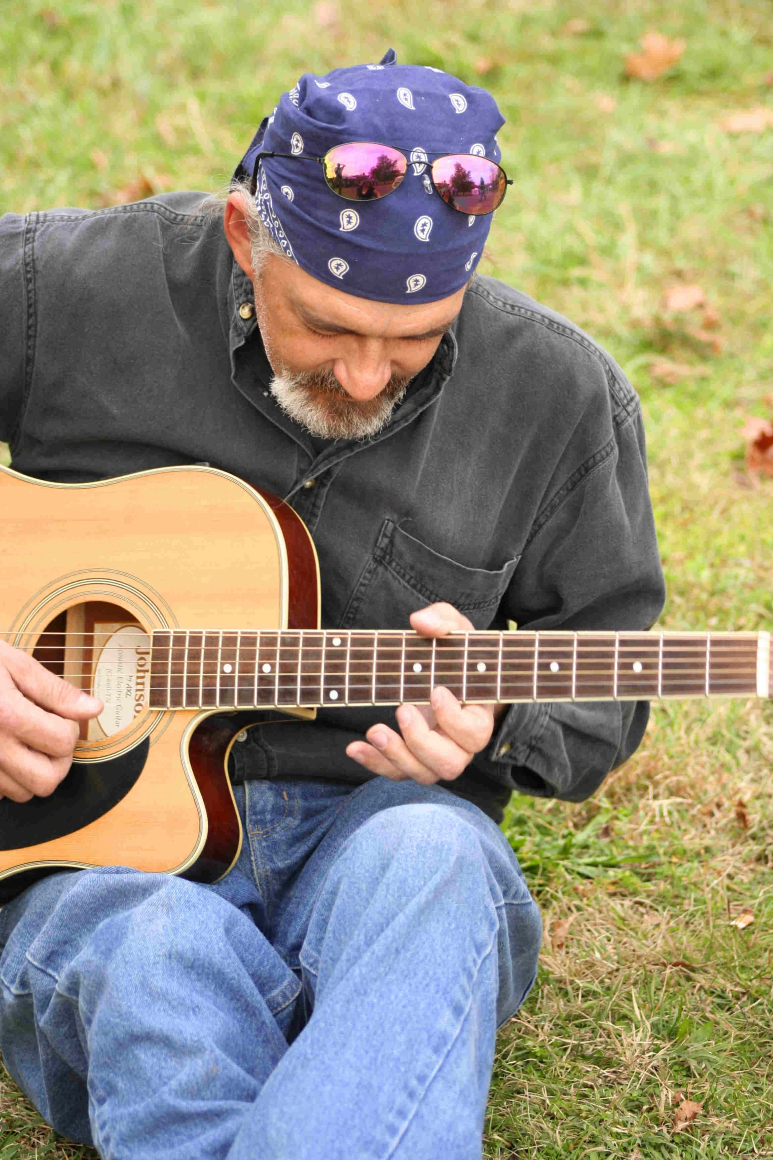 an older man sits on the grass playing a guitar