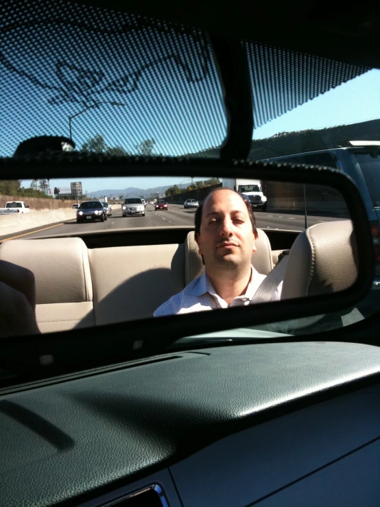 a man in the passenger seat of his car looks in the mirror