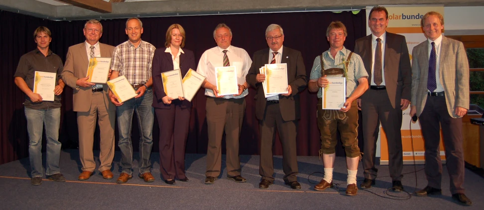 six men standing on stage holding paper work pieces