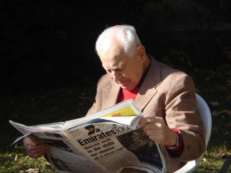 an old man sitting on a chair reading a newspaper