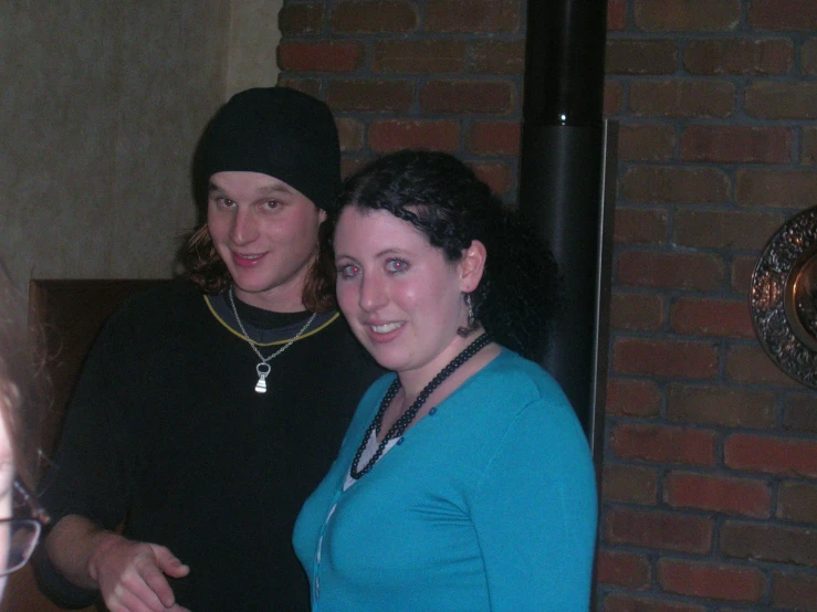 two friends smile at the camera, with a brick wall in the background