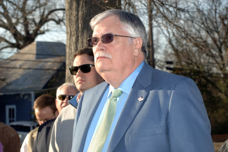 older gentleman wearing sunglasses standing outside with others