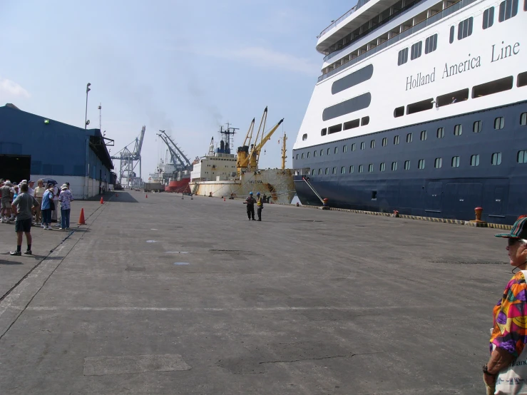 people walking around on a pavement in front of large ships