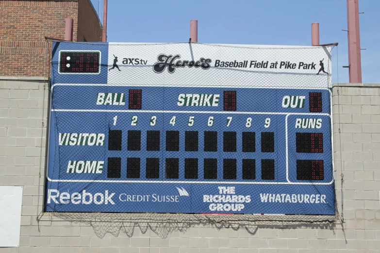 a scoreboard behind the brick wall of a ball park