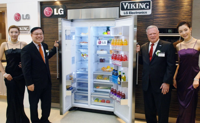 three men and two women in suits stand beside a refrigerator