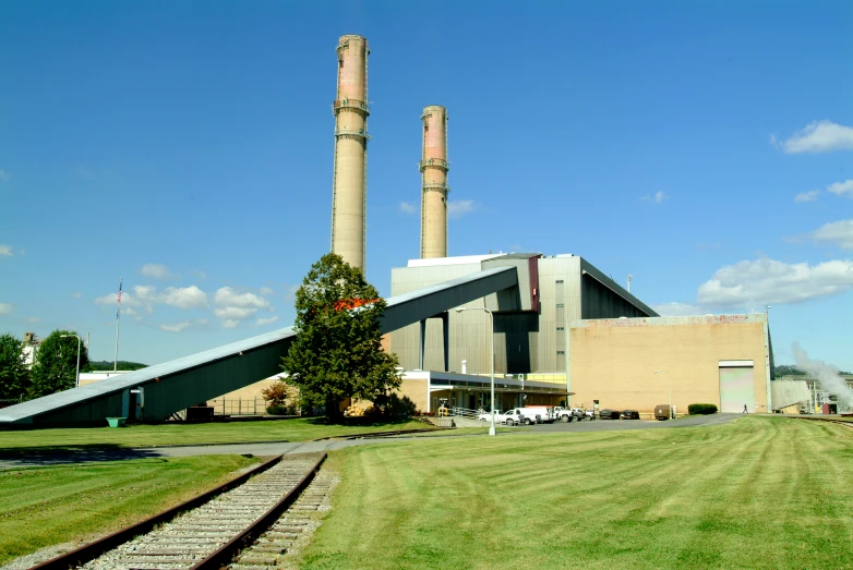 a large industrial building sits in the middle of a grass field with several rails leading into it