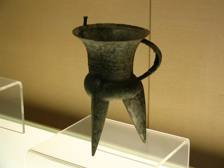 a metal vase sits on display on a small pedestal