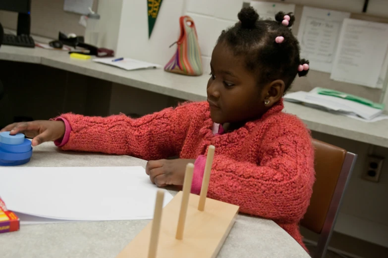 a little girl sits at the table doing some craft work