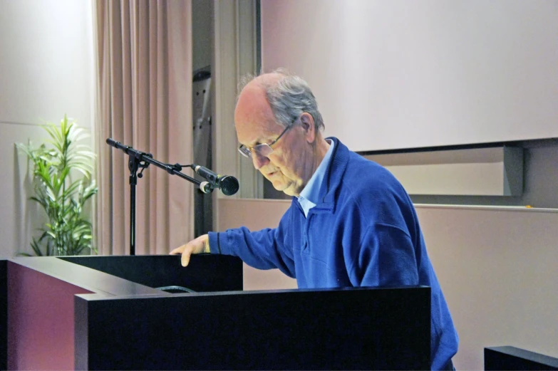 an older man standing at a podium and holding a book