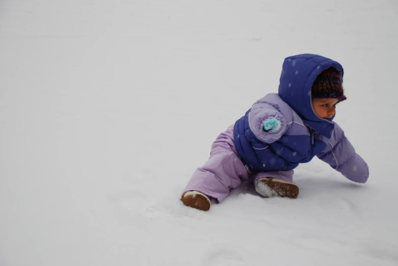 a toddler in a purple winter coat sliding down snow