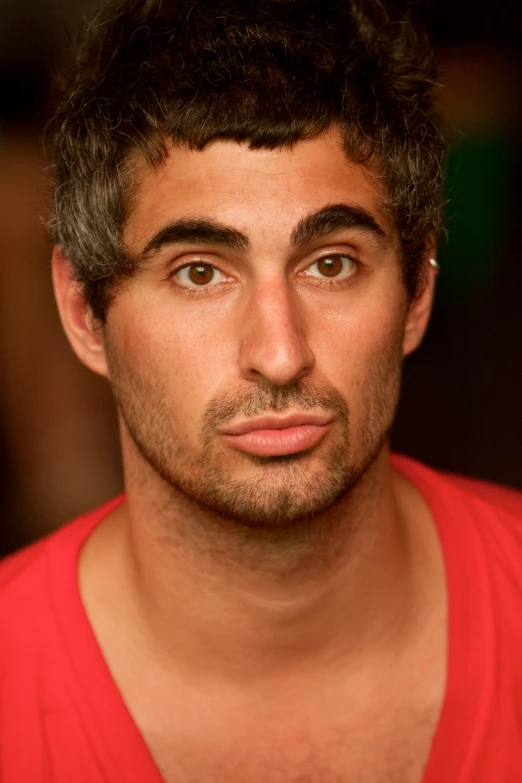 a man looks directly into the camera while wearing a red shirt