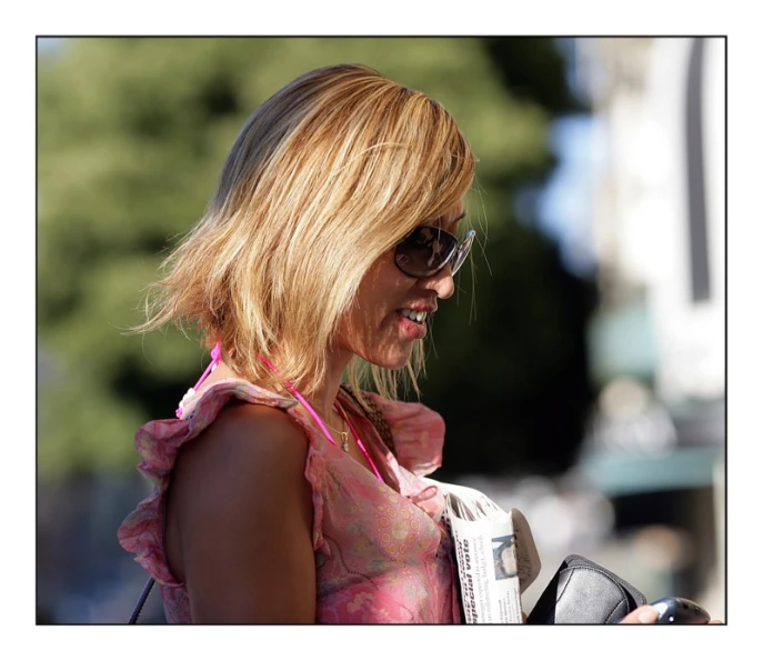 a woman wearing sunglasses walking with a cell phone