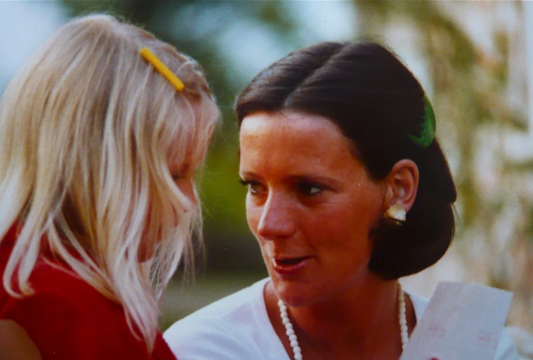 a woman wearing pearl necklace talking to another woman