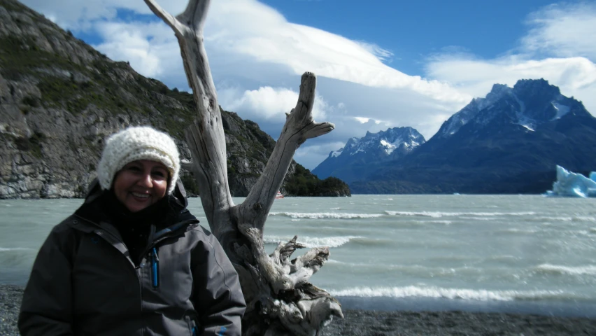 a man standing near the water and snow capped mountains