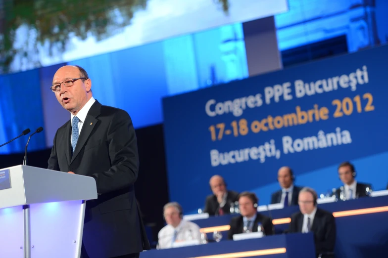 the man stands in front of a microphone at a political conference