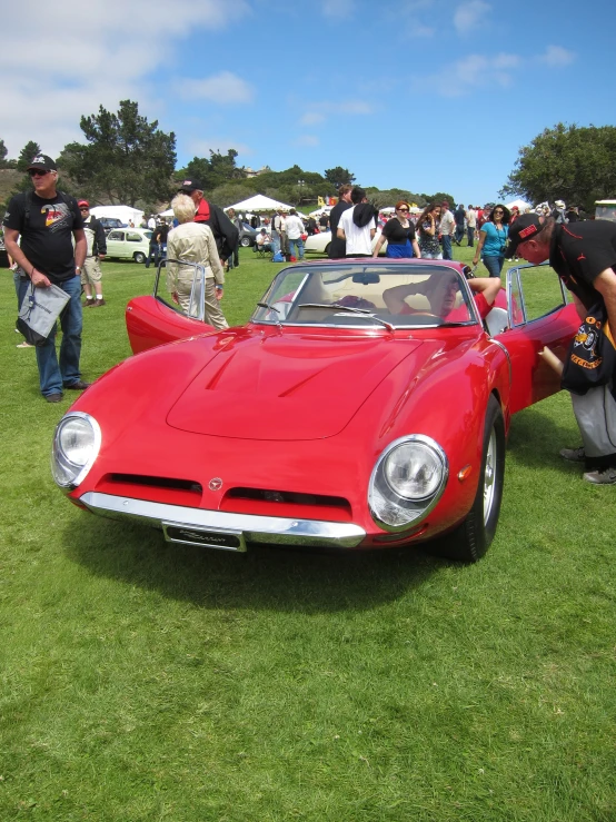 an old style red sports car in the middle of some grass