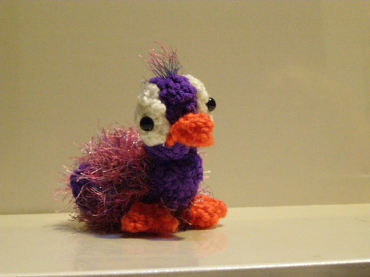 a crochet purple and orange bird sitting on top of a table