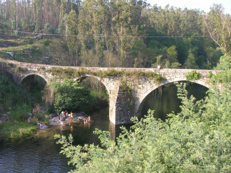 an old bridge with people swimming in the river