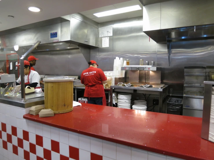two men standing behind a red counter in a commercial kitchen