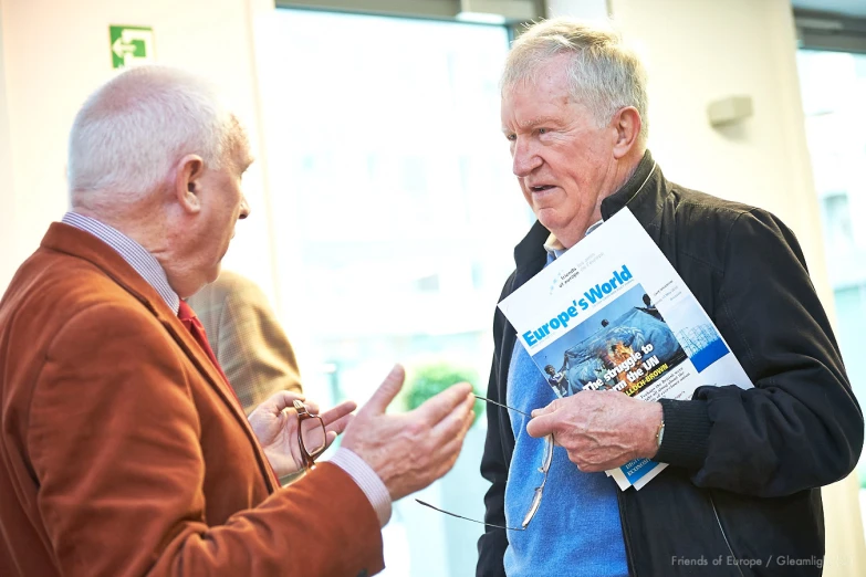 two men are talking while holding papers and one is looking at them