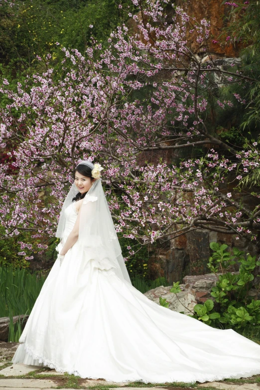 a woman wearing a wedding dress and a veil poses in front of flowers