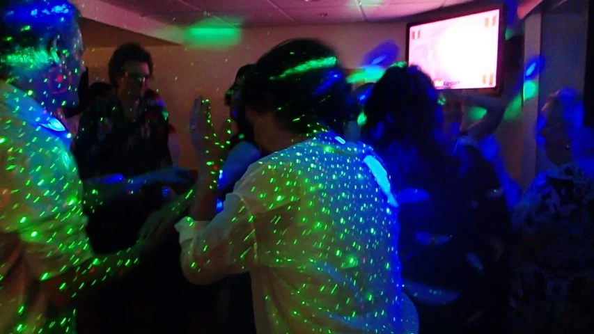 a large group of people dancing with green and blue light up lasers on their arms