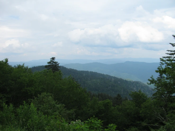 the mountains are full of green trees and clouds