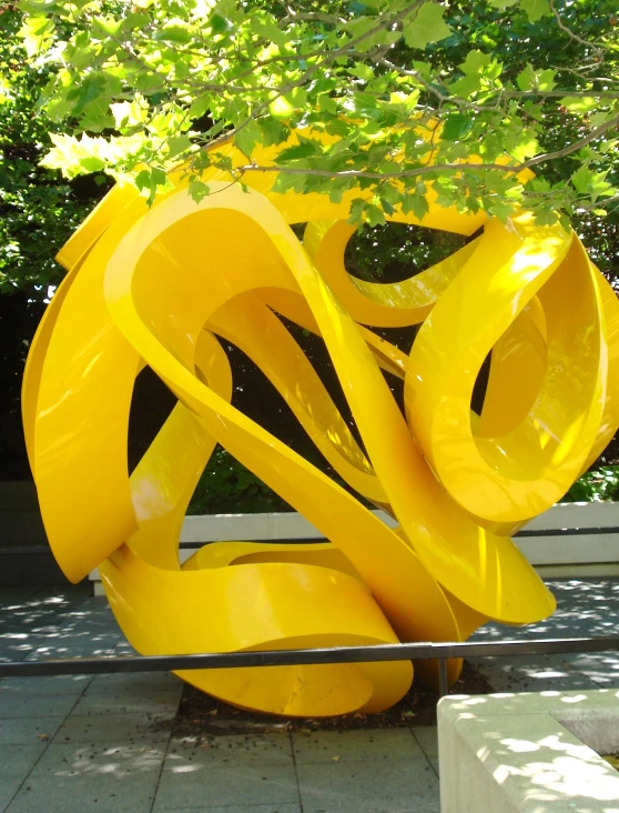 a yellow sculpture on a white bench with trees in the background