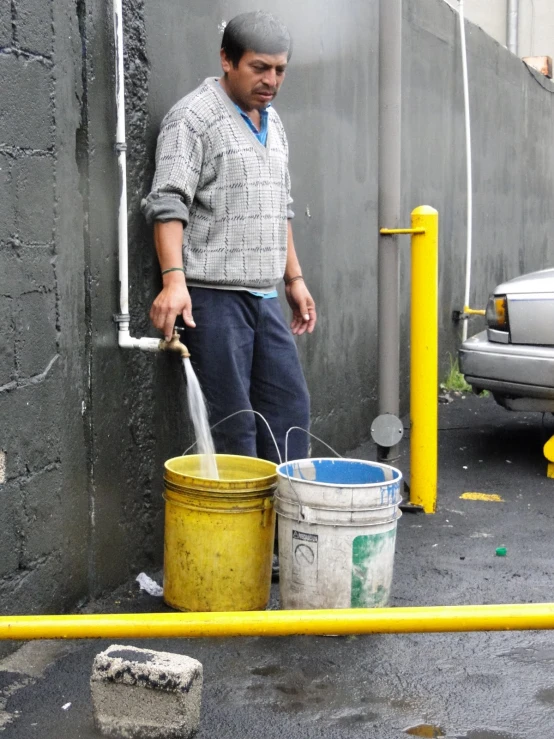 a man standing next to a yellow barrel pouring water into two buckets