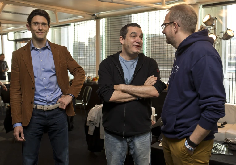 three men talking in an office cubicle with large windows