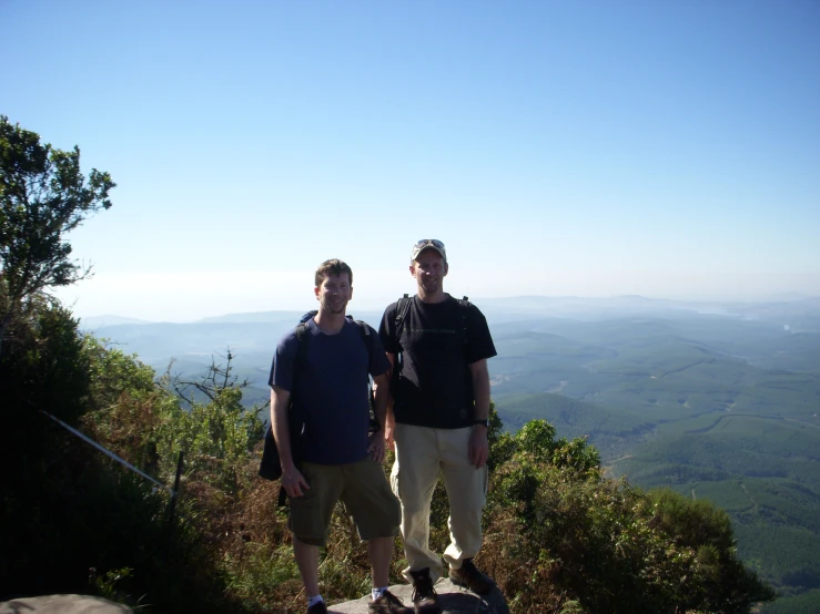 two men standing in front of a hill, on top of a hill