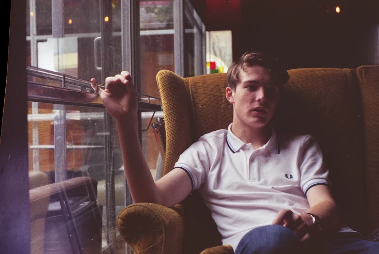 a man sits in an armchair with his arm up and his face looking out the window