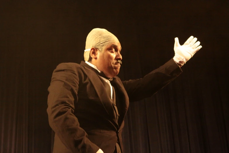man in tuxedo and head scarf on stage with arms extended and folded out