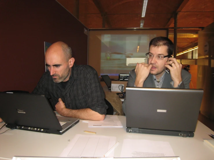 two men working on their laptops in an office