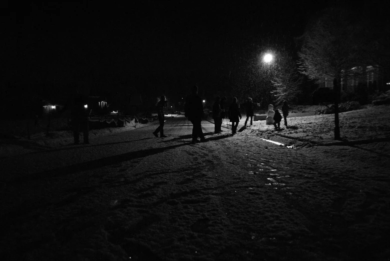 the silhouette of several people walking in a line on snow at night