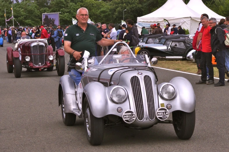 an old style race car with people in it and a large tent